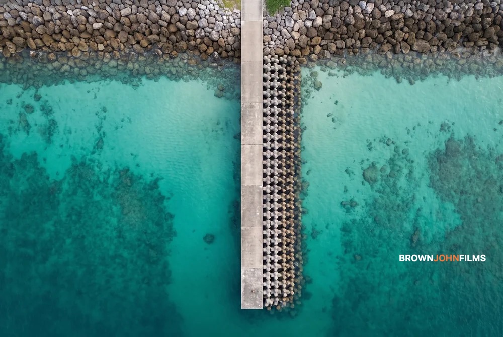 Concrete breakwater dividing turquoise shallows, seen from directly above